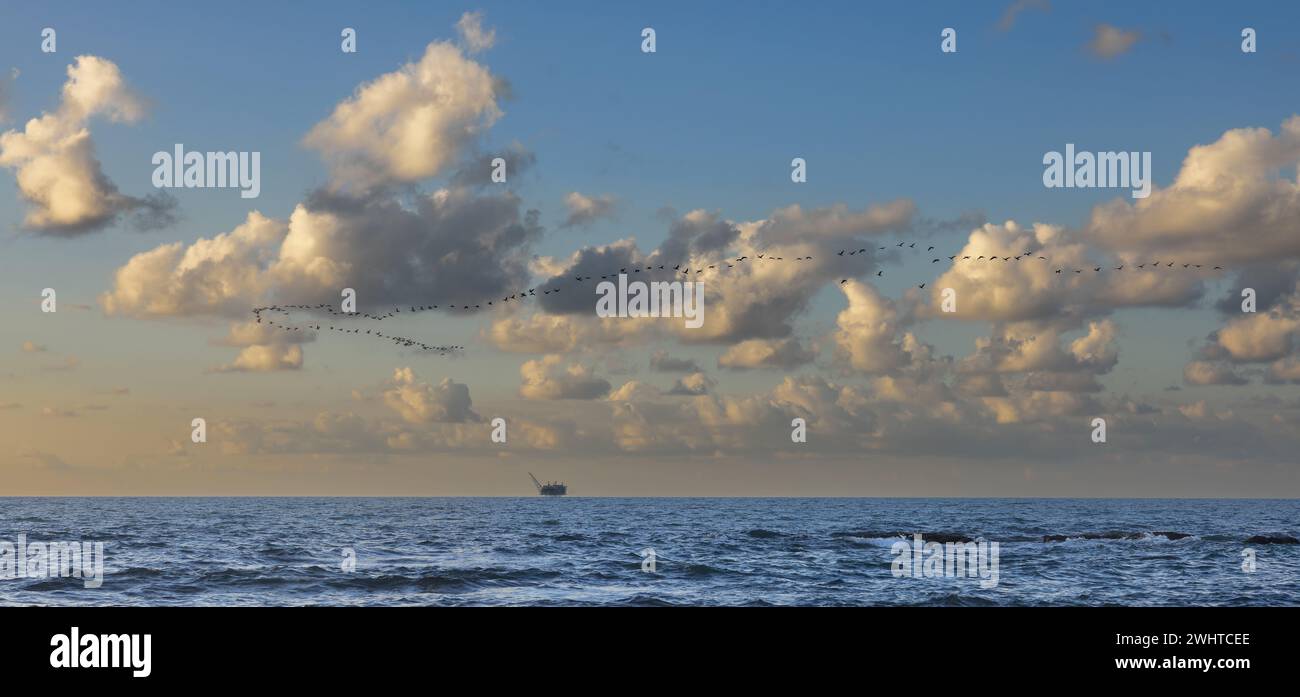 view of an offshore gas platform against the backdrop of a flock of cranes in the clouds Stock Photo