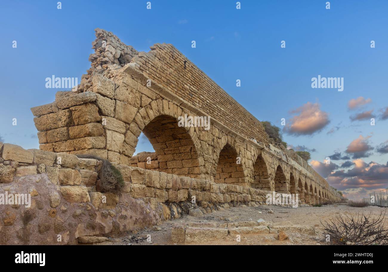 old Aqueduct built by the Romans against the sky at sunset in Caesarea Israel Stock Photo