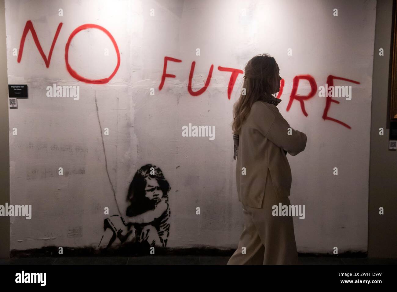 Moscow, Russia. 10th of February, 2024. A woman stands before 'No Future' painting on display during an exhibition dedicated to English-based street artist Banksy, in Moscow, Russia. Titled 'Find Banksy' and held at VDNKH Pavilion No 21, it contains copies of the original works by Banksy Stock Photo