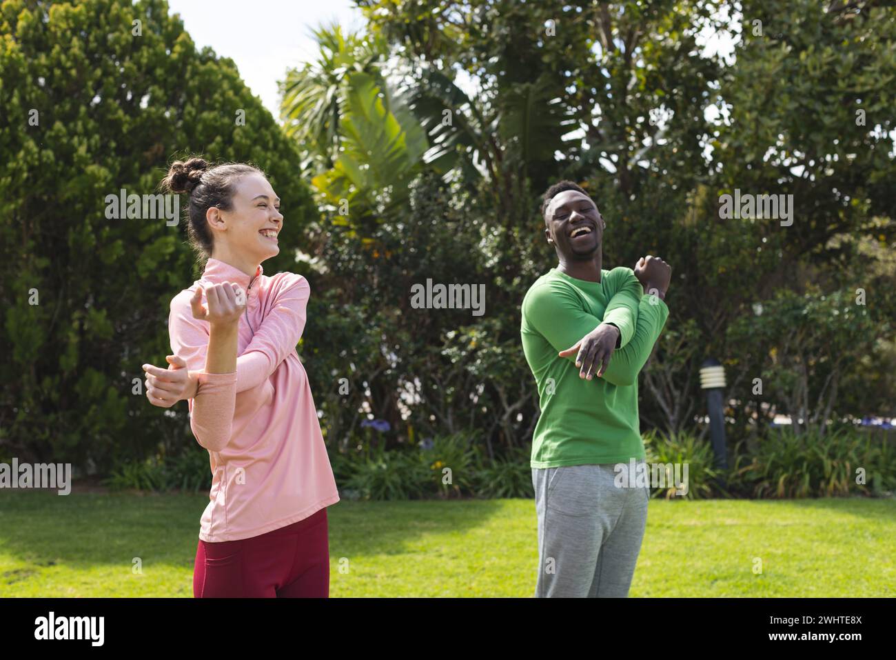 Happy diverse couple practicing yoga and stretching in garden Stock Photo