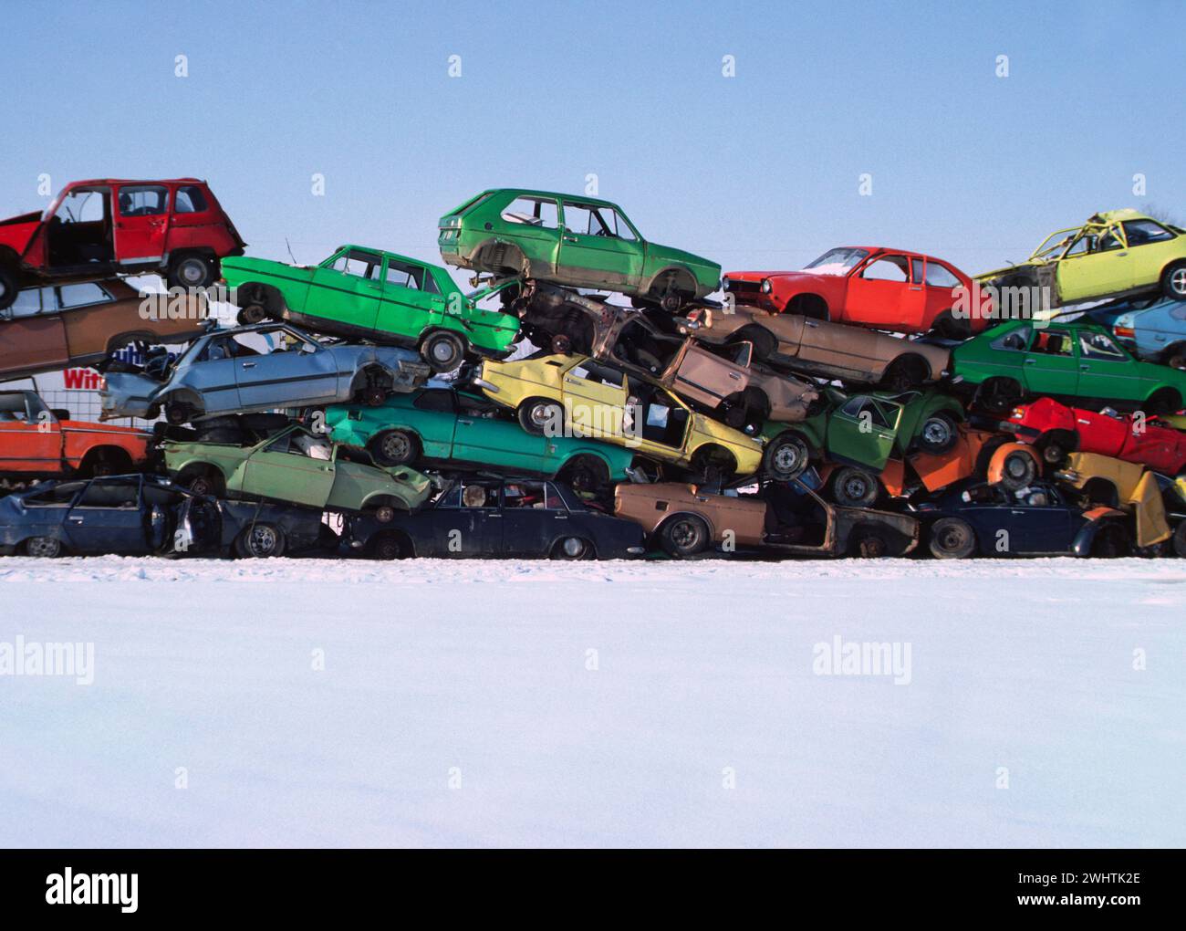 alte Autos in bunten Farben auf einem Schrottplatz im Winter * * colorful pile of wrecked cars on snow white ground Stock Photo
