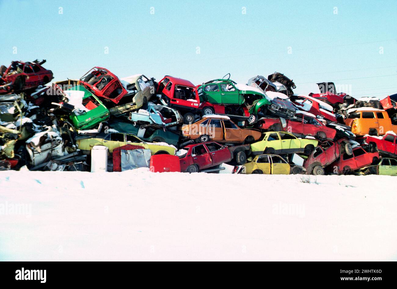 alte Autos in bunten Farben aufgetürmt auf einem Schrottplatz im Winter * colorful pile of wrecked cars on snow area Stock Photo