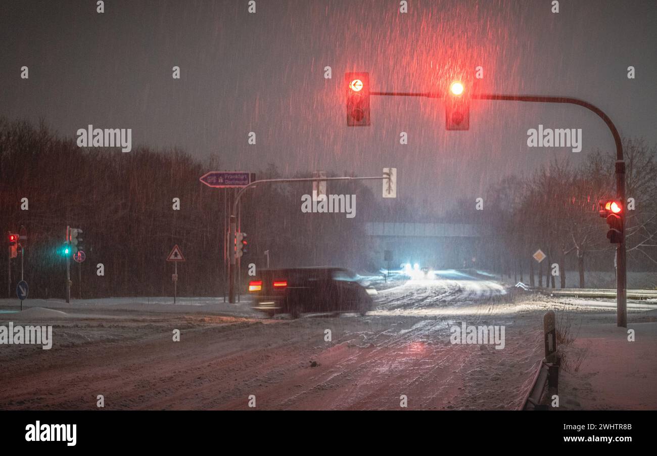 Red traffic lights suspended above a street on a snowy, dark day Stock Photo