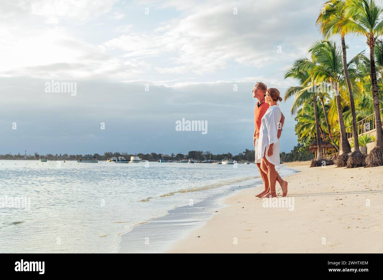 Couple in love hugging on sandy exotic beach while having evening walk by Trou-aux-Biches seashore on Mauritius island enjoying sunset. People relatio Stock Photo