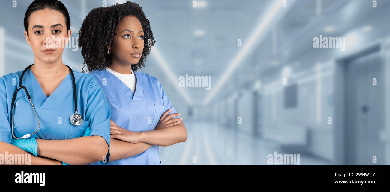 Two serious female nurses in blue scrubs with crossed arms and ...