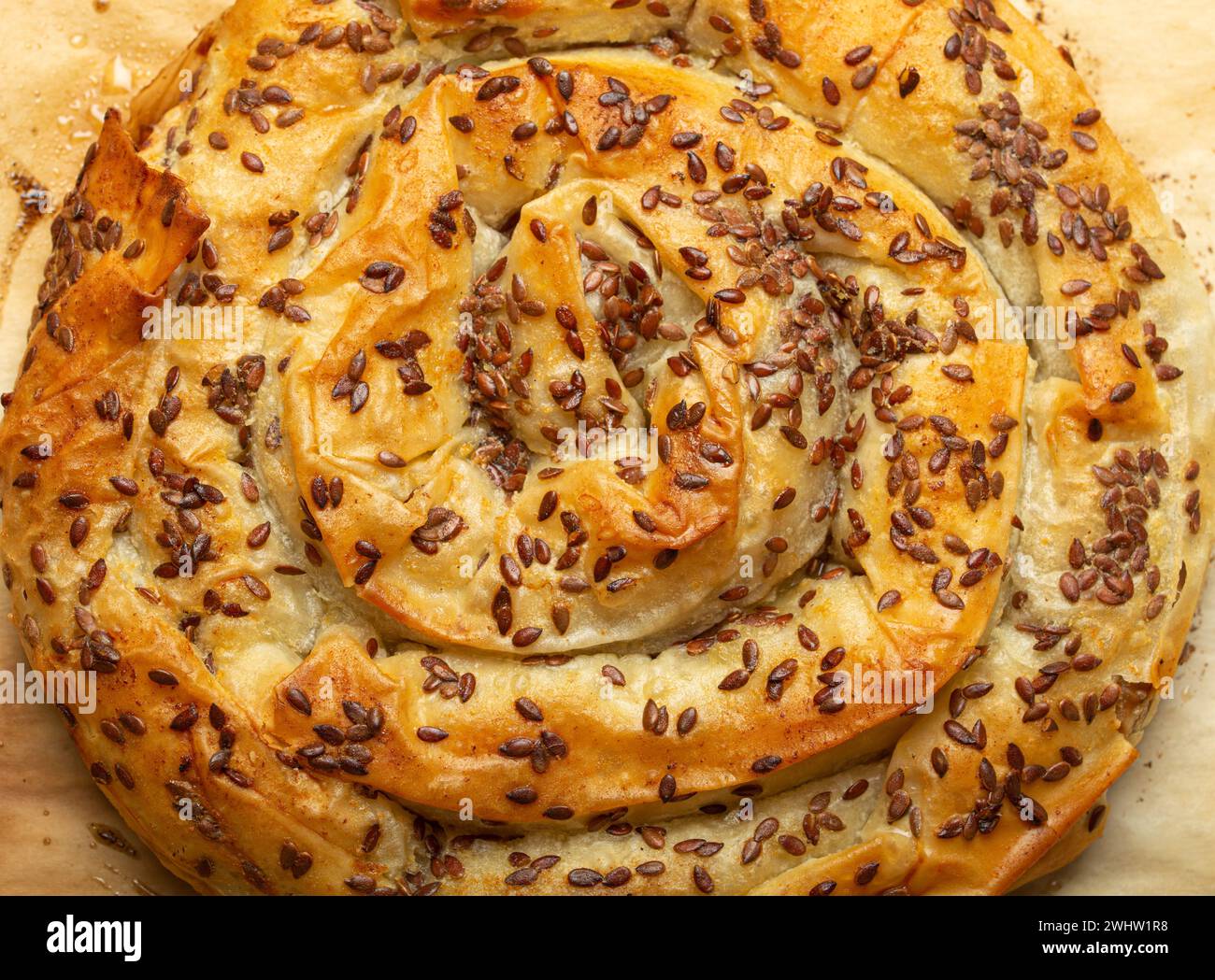 Freshly baked Burek made of filo dough with filling on baking paper background top view. Traditional savoury spiral pie of Balka Stock Photo