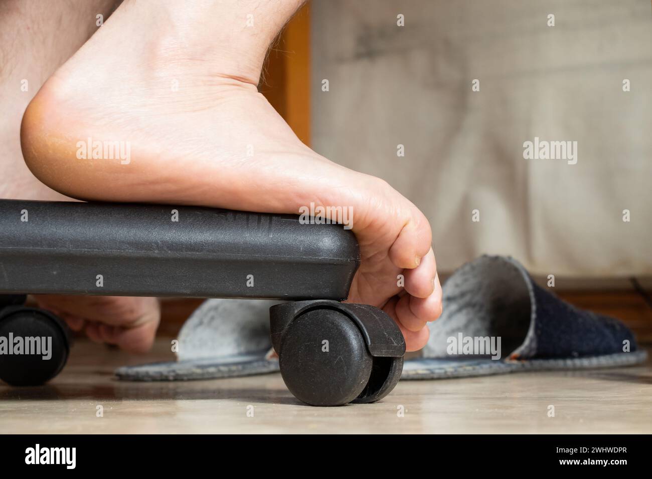 Male leg on a chair at home under the table, male foot close-up Stock Photo