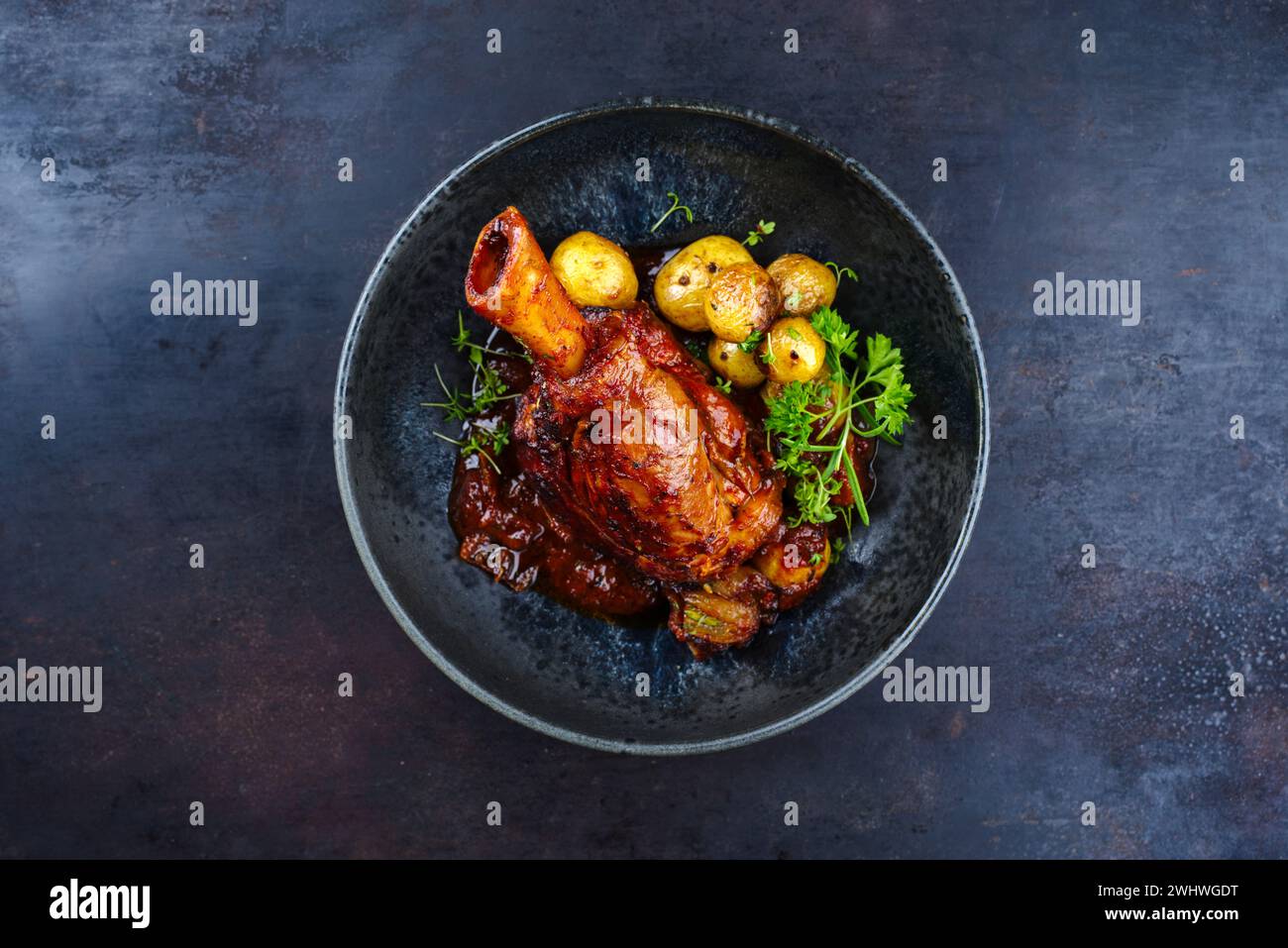 Traditional braised slow cooked lamb knuckle in red wine sauce with mini roast potatoes and