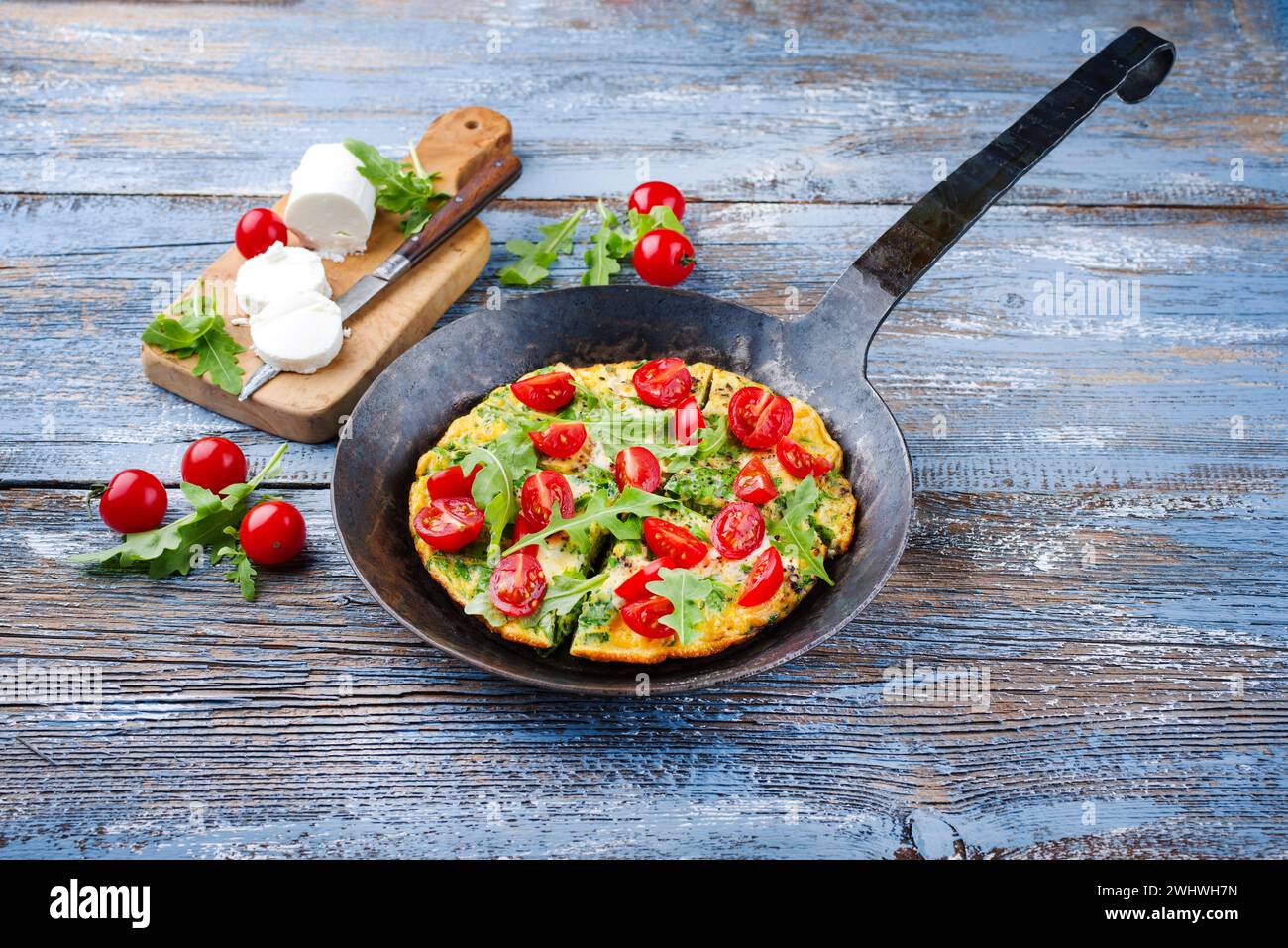 Traditional German vegetarian rucola omelet with cherry tomatoes and cream goat cheese served as close-up in a wrought iron fryi Stock Photo