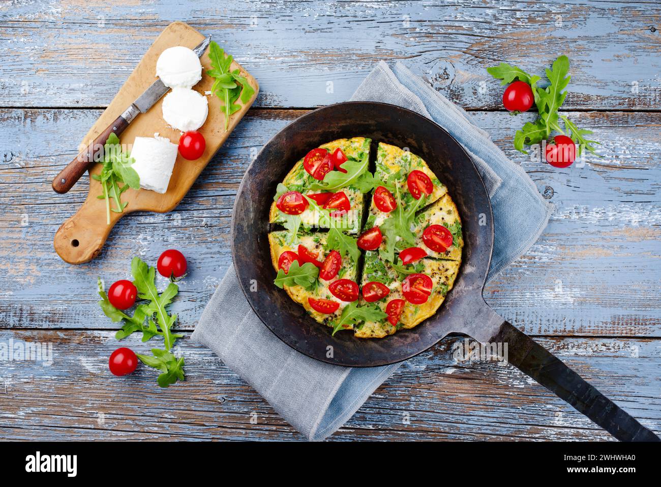 Traditional German vegetarian rucola omelet with cherry tomatoes and cream goat cheese served as top view in a wrought iron fryi Stock Photo