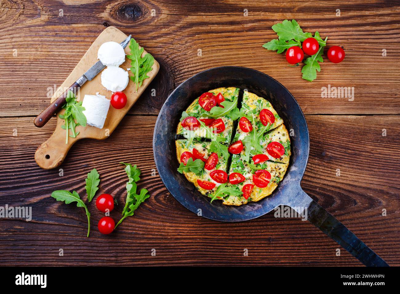 Traditional German vegetarian rucola omelet with cherry tomatoes and cream goat cheese served as top view in a wrought iron fryi Stock Photo