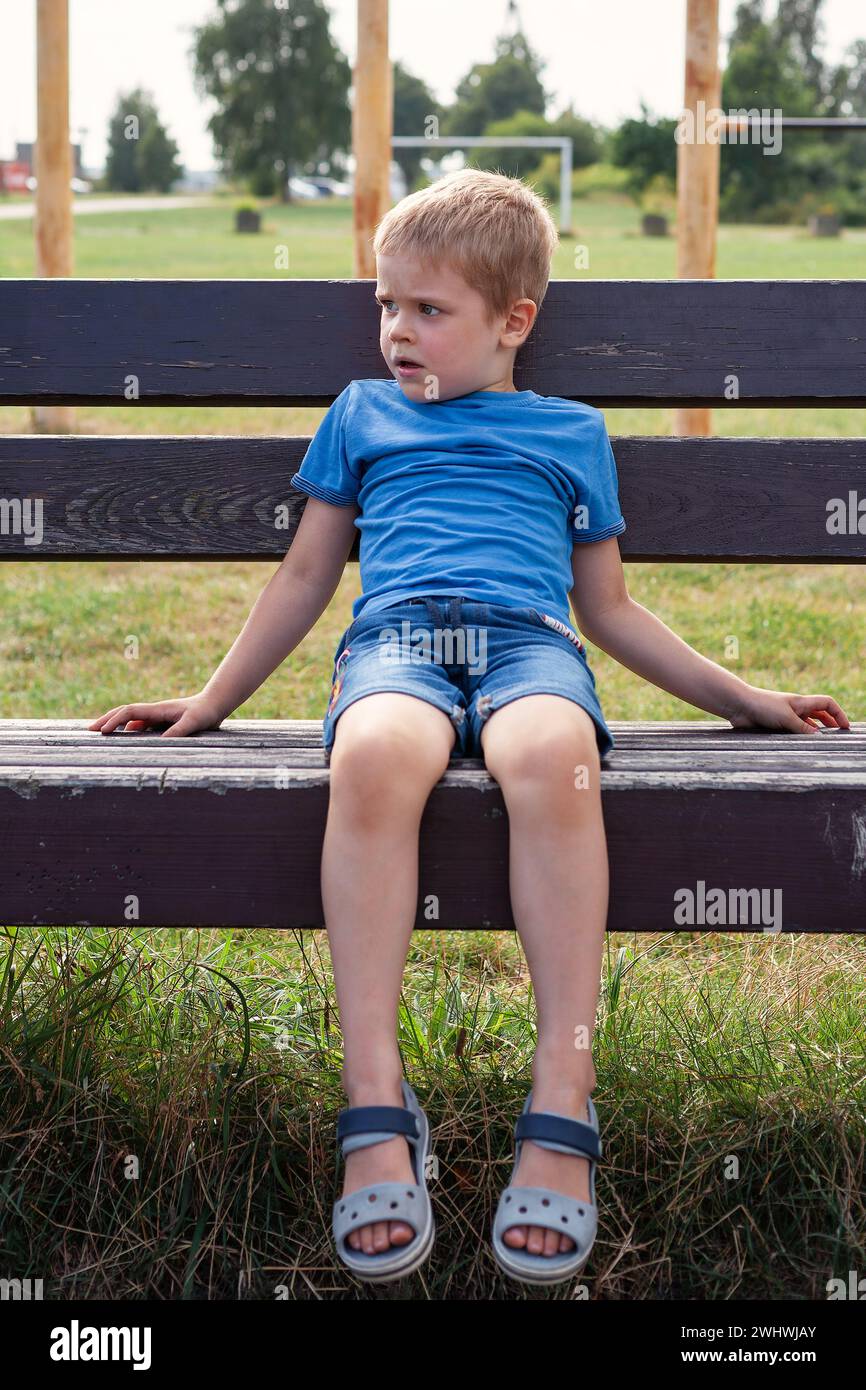 Lonely bored boy sitting on bench. Sad mood in child depression concept. Stock Photo