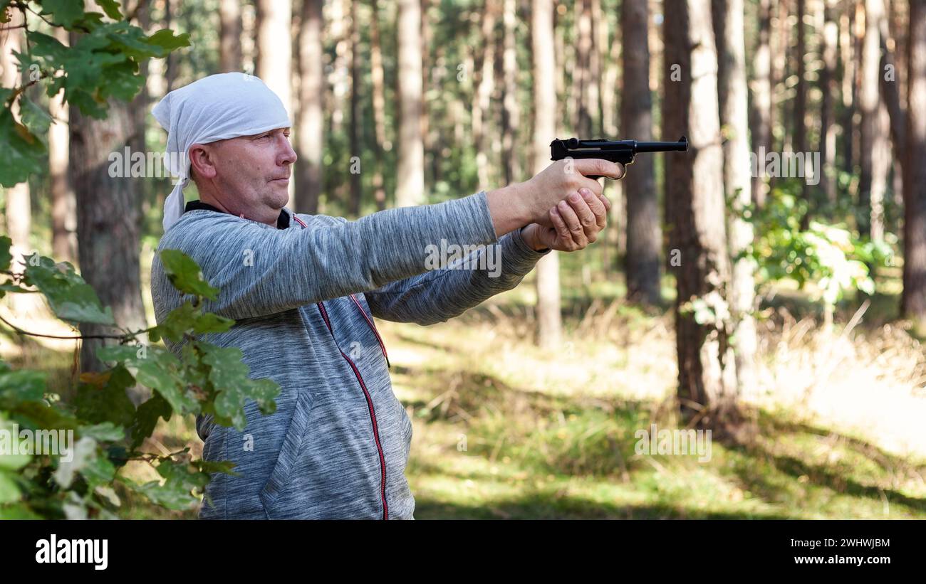 A man in the woods on a sunny summer day having fun and learning to shoot at a target with his German air pistol. Stock Photo