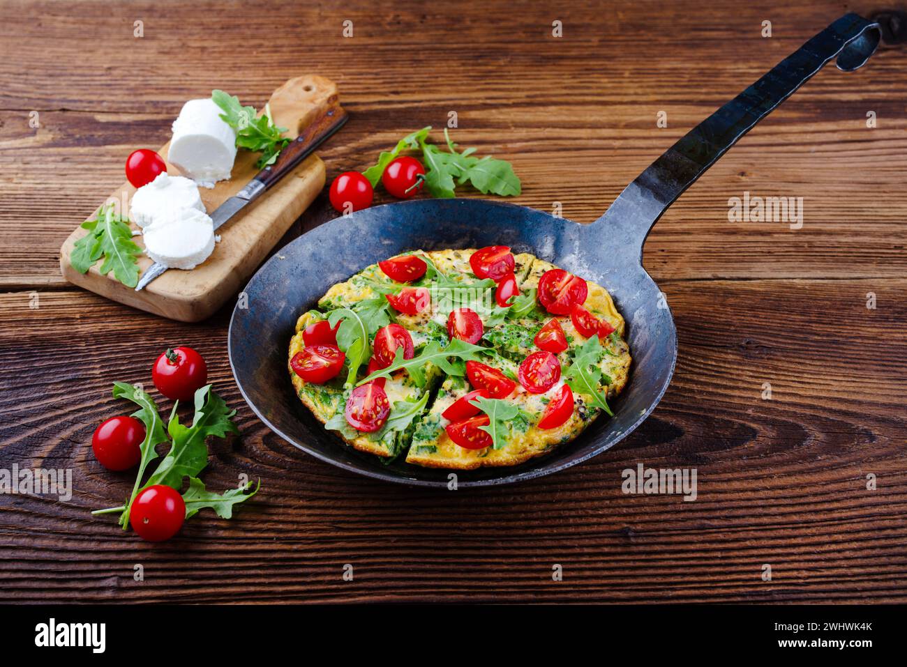 Traditional German vegetarian rucola omelet with cherry tomatoes and cream goat cheese served as close-up in a wrought iron fryi Stock Photo