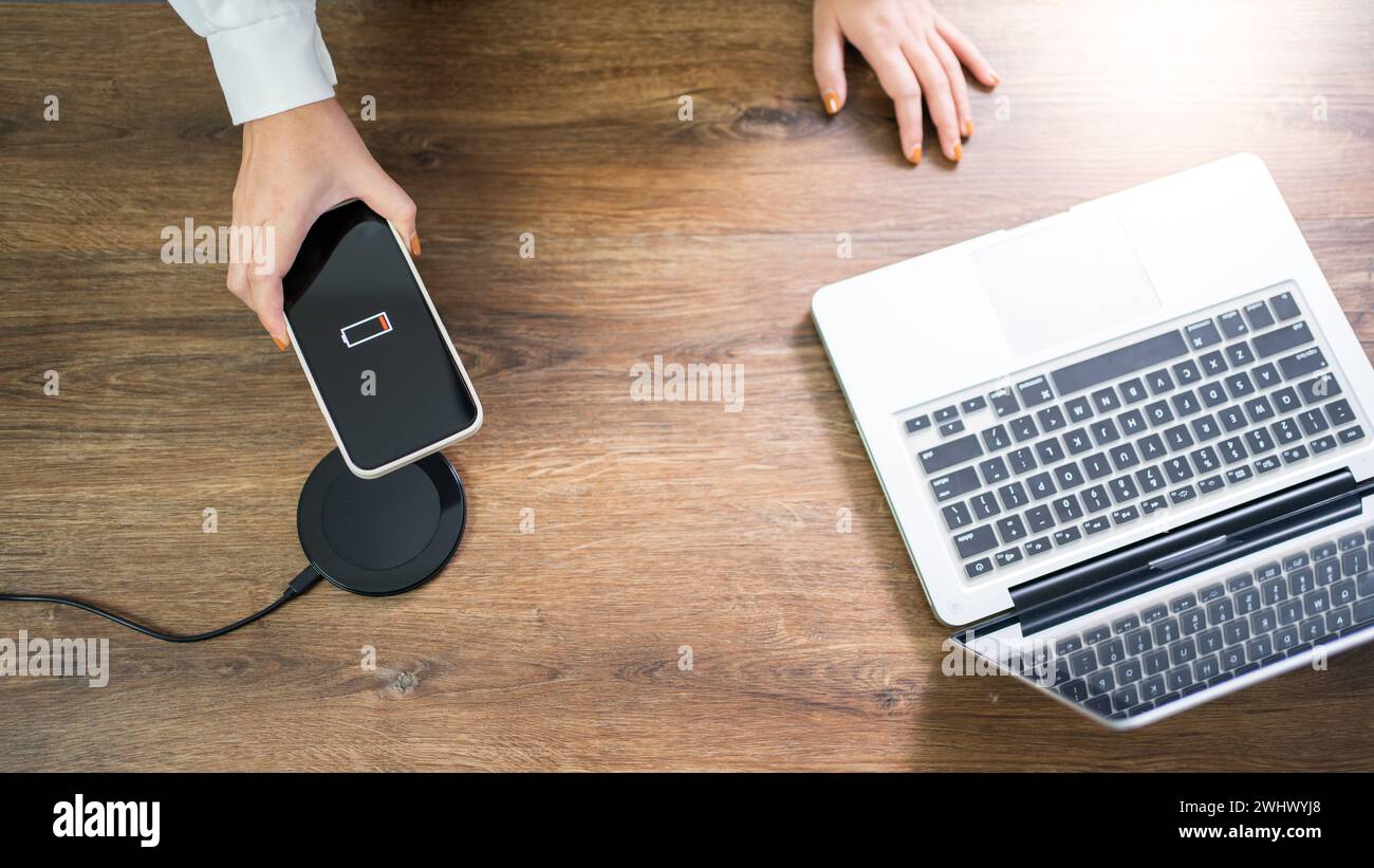Charging mobile phone battery with wireless charging device in the table. Smartphone charging on a charging pad. Mobile phone ne Stock Photo