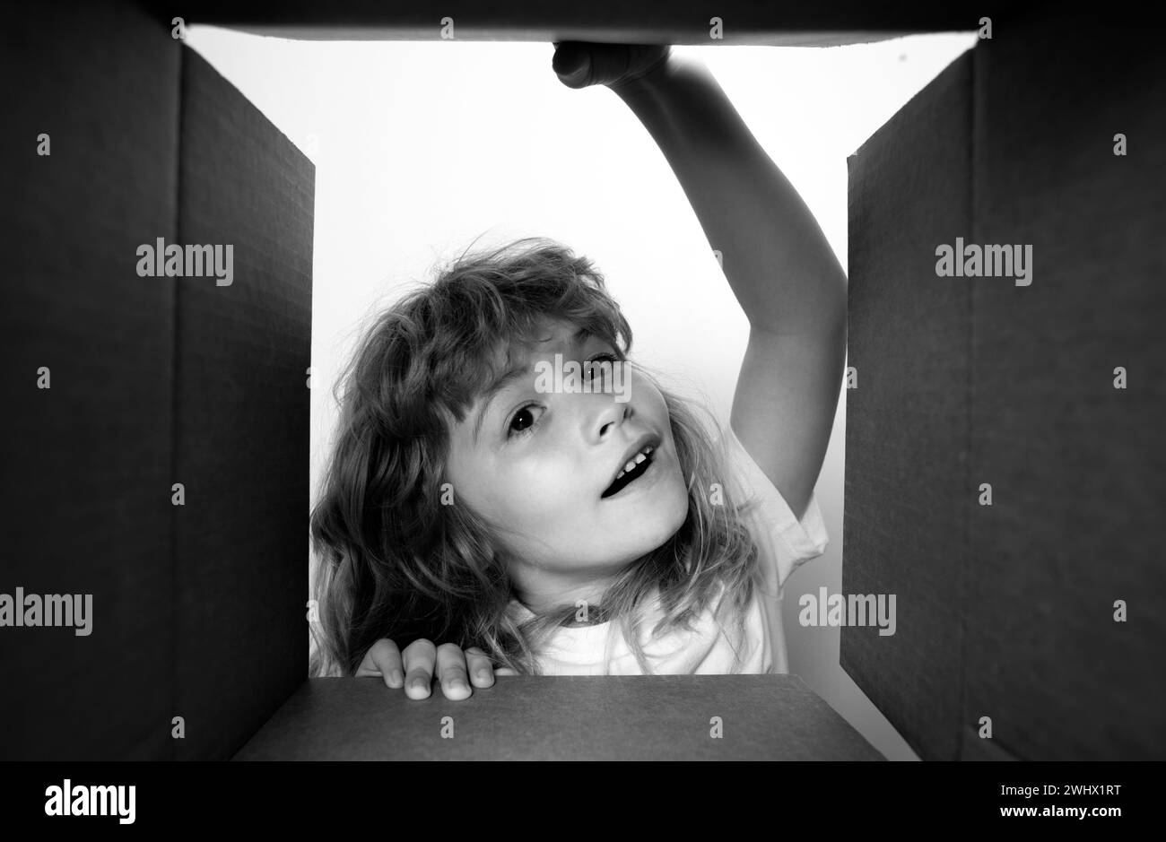 Kid unpacking and opening carton box, and looking inside with surprise face. Unpacking cardboard box for kids. Stock Photo