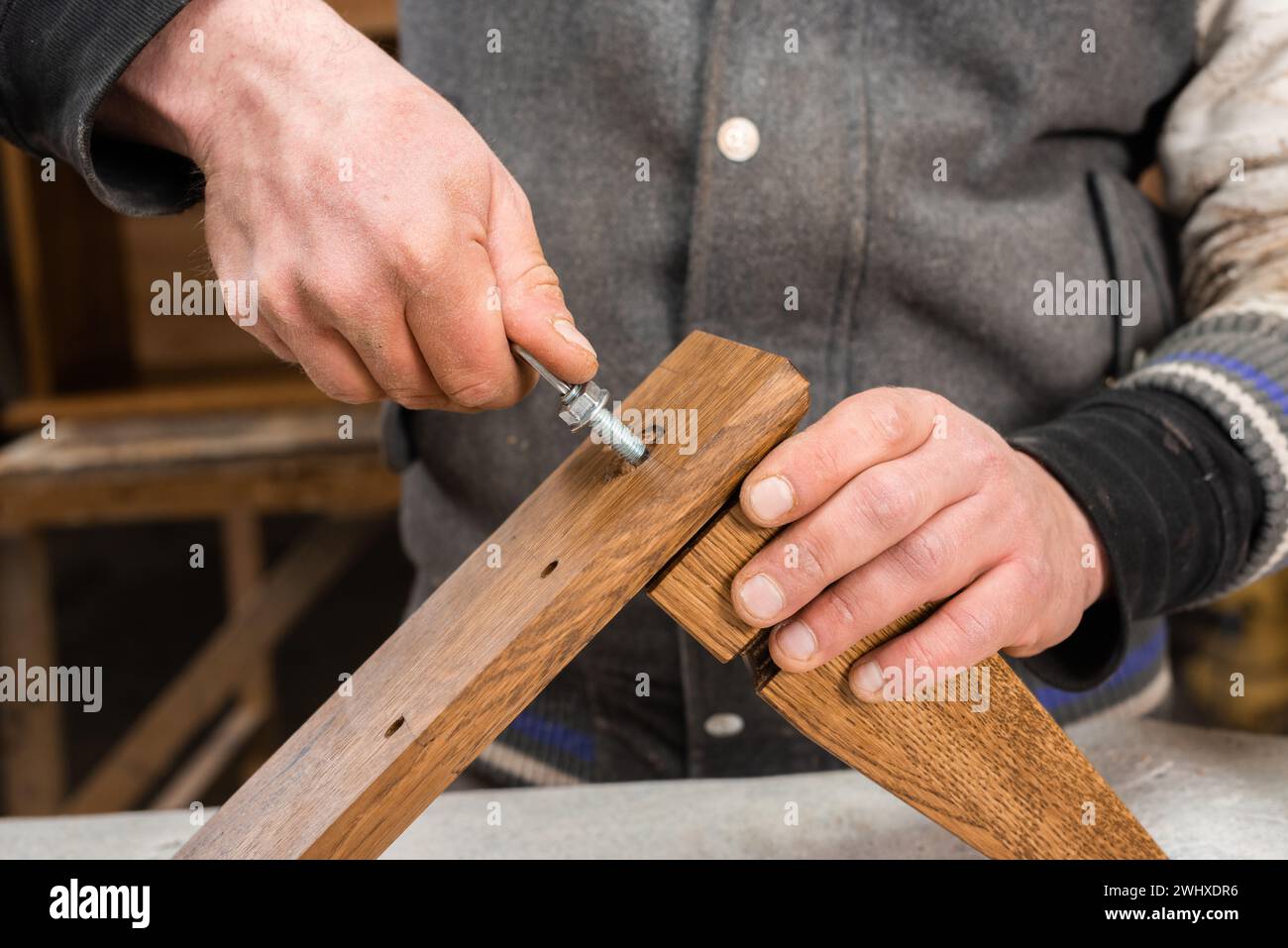 The carpenter screws a bolt into the leg of the cabinet closeup Stock Photo
