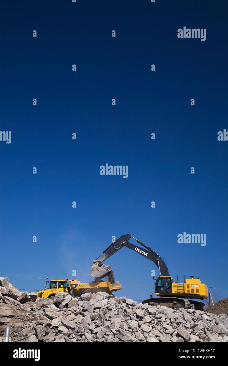 Deere 450D excavator scooping and loading large dynamited rocks onto a ...