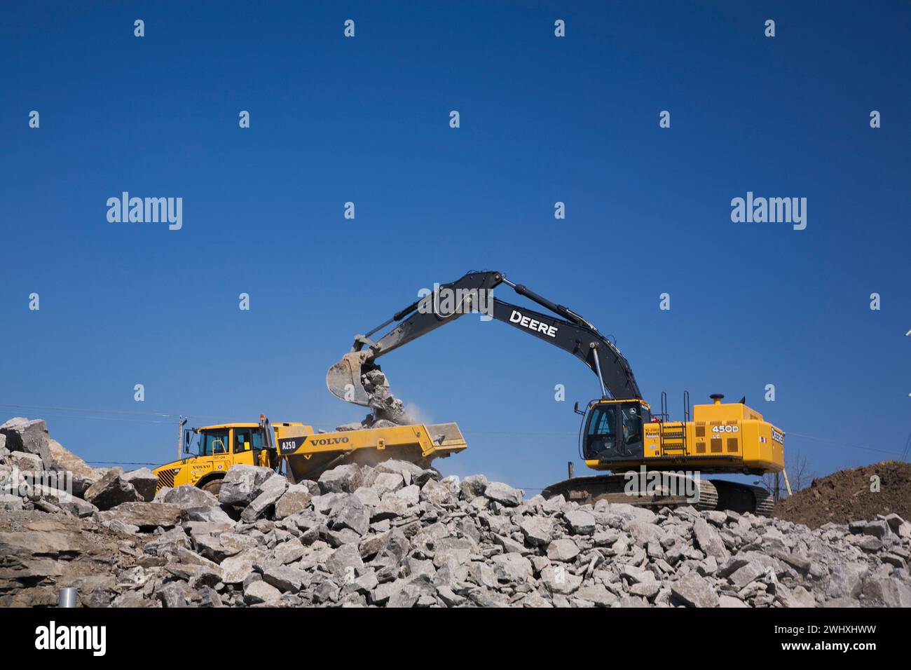 Deere 450D excavator scooping and loading large dynamited rocks onto a ...