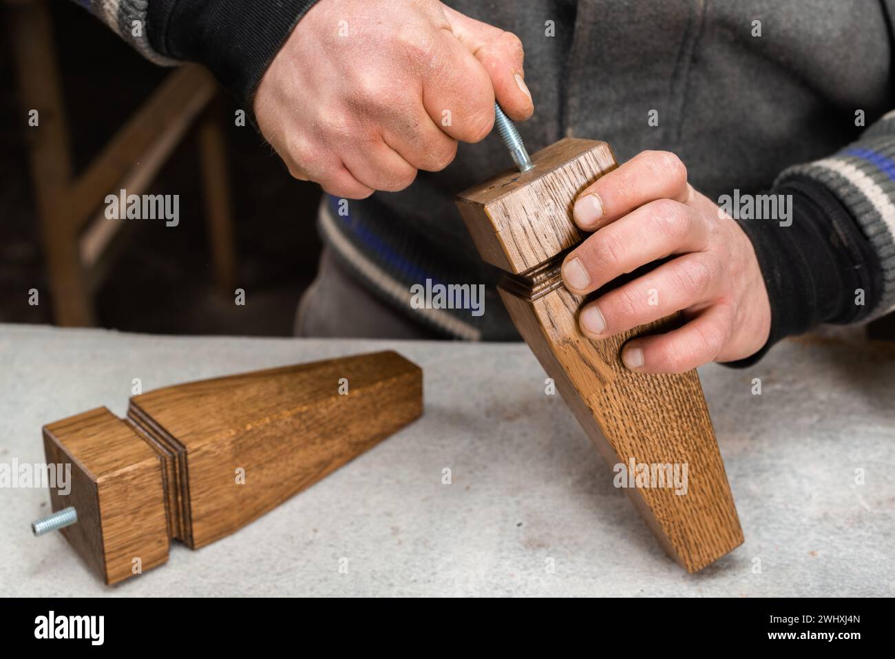 The carpenter screws the mount into the cabinet leg closeup Stock Photo