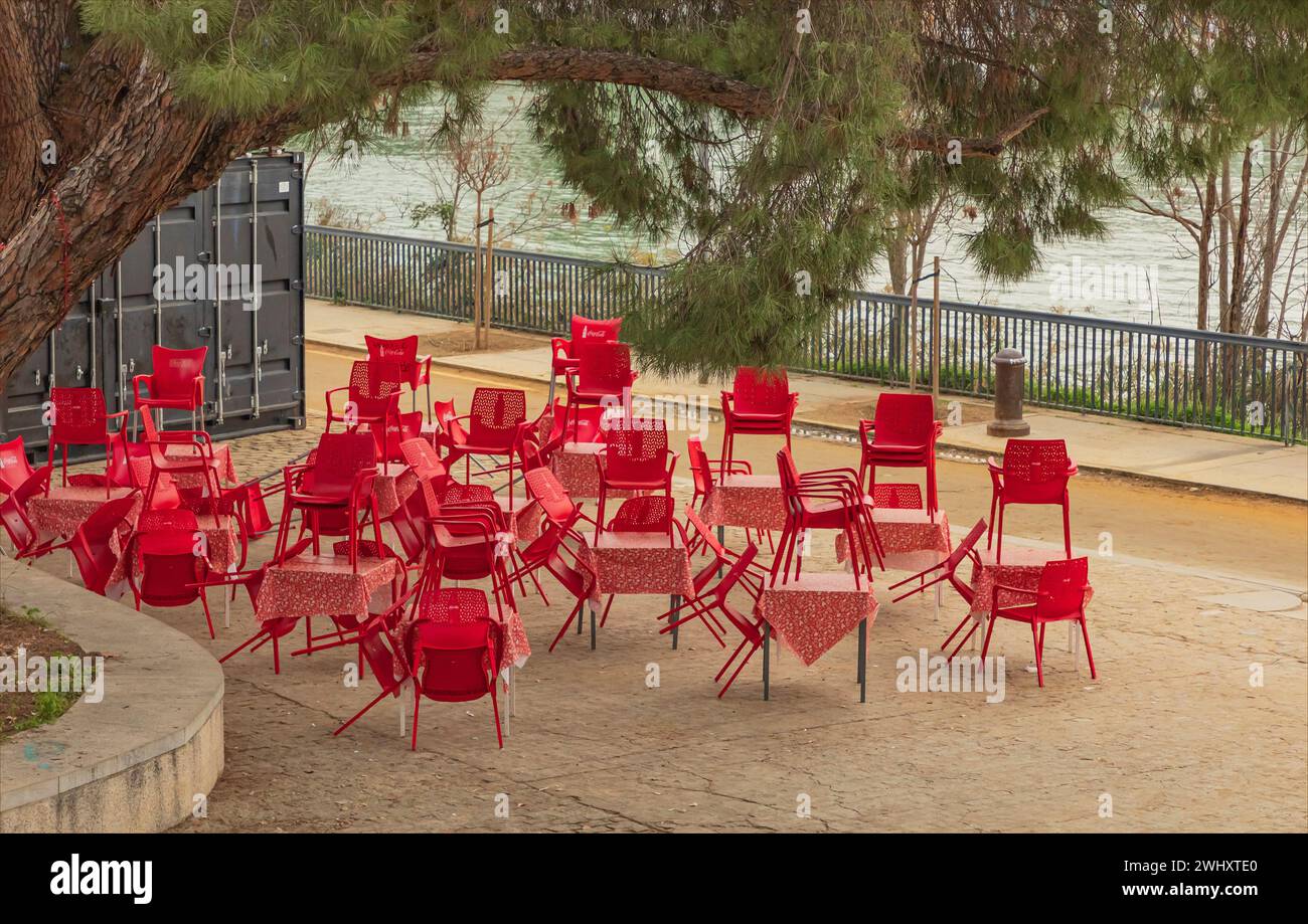 Red tables  with table cloths and chairs stacked up by a river Stock Photo