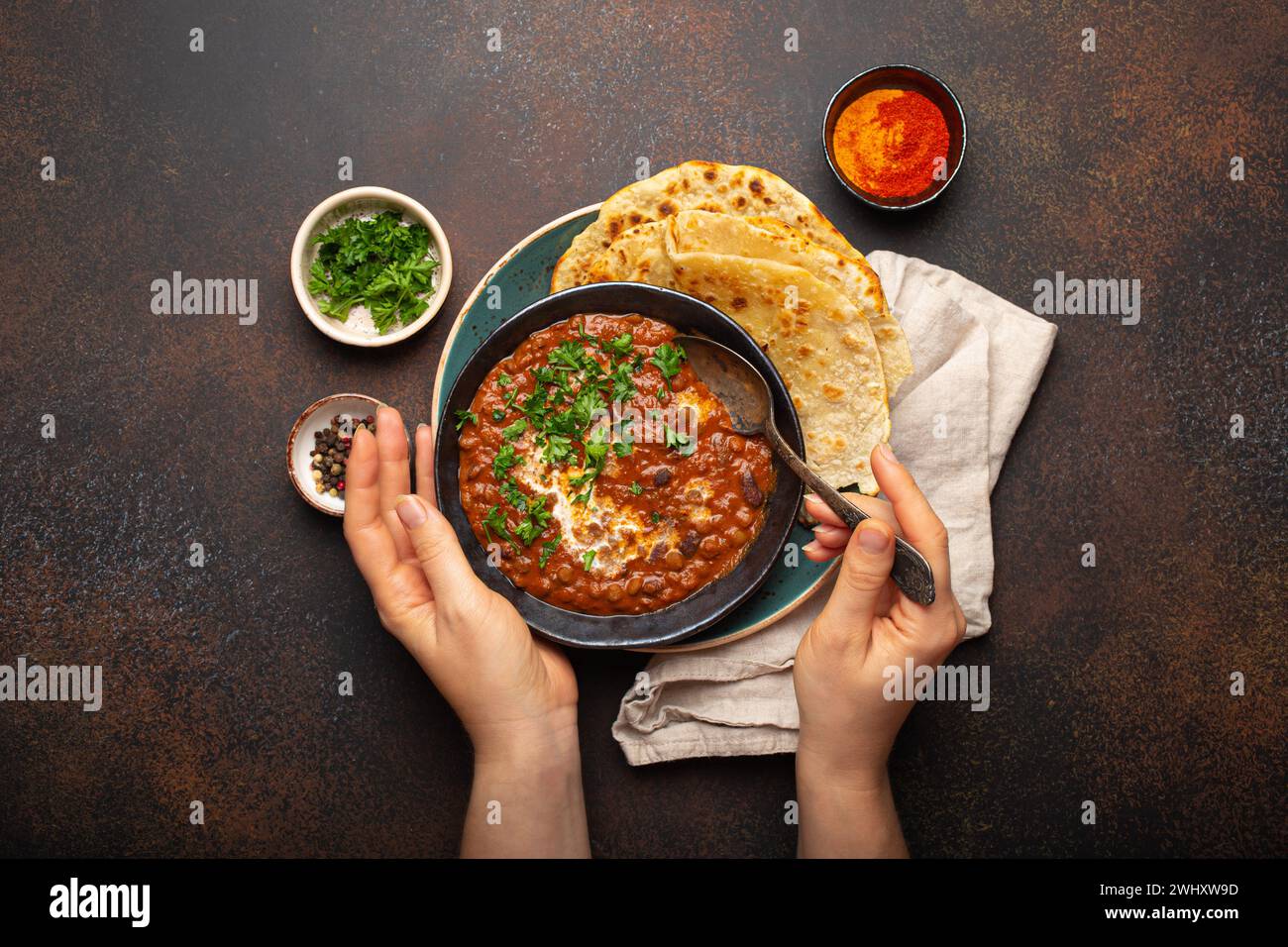 Female hands holding a bowl and eating traditional Indian Punjabi dish Dal makhani with lentils and beans served with naan flat Stock Photo