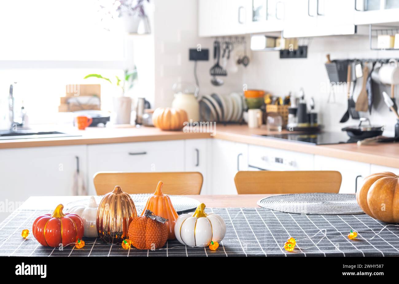 Decor of white classic kitchen with pumpkins, garlands, latern for Halloween and harvest with figurine of house. Autumn mood in Stock Photo