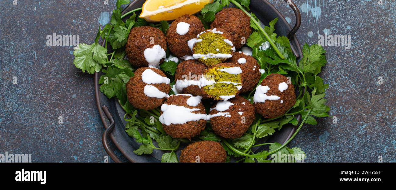 Plate of fried falafel balls served with fresh green cilantro and lemon, top view on rustic concrete background. Traditional veg Stock Photo