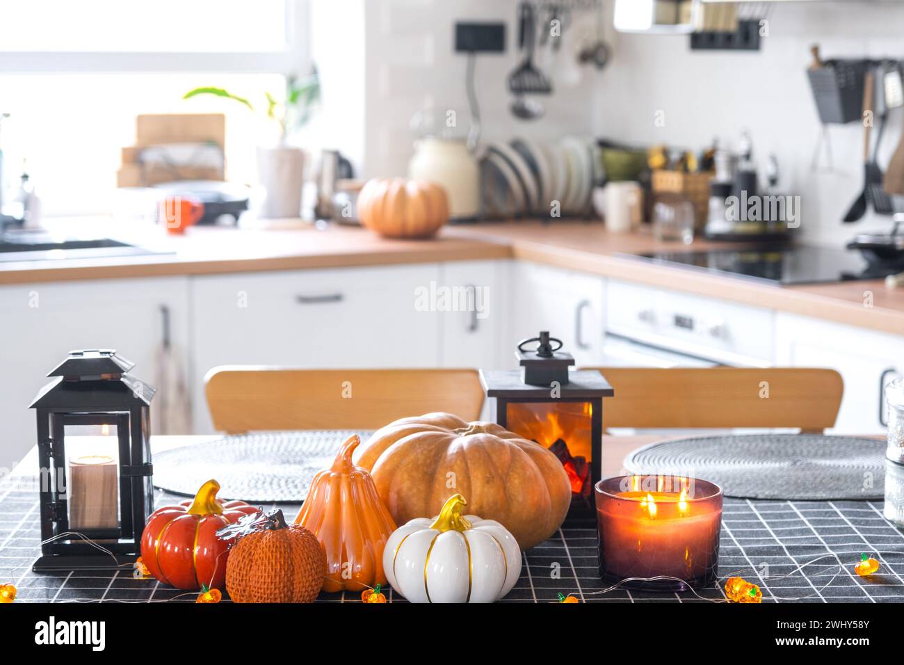 Decor of white classic kitchen with pumpkins, garlands, latern for Halloween and harvest with figurine of house. Autumn mood in Stock Photo