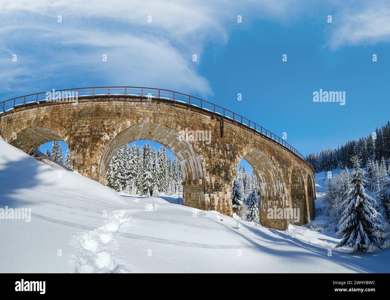 Stone viaduct (arch bridge) on railway through mountain snowy fir forest. Snow drifts  on wayside and hoarfrost on trees and ele Stock Photo