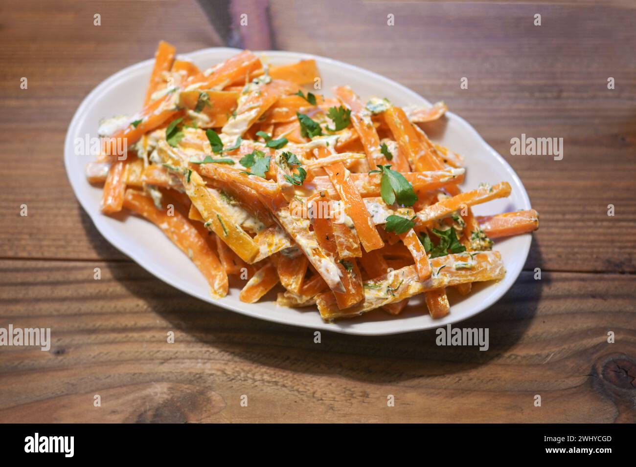 Hot carrot strips with a creamy spicy dressing and parsley garnish, healthy cold tapa snack for a Mediterranean buffet on a rust Stock Photo