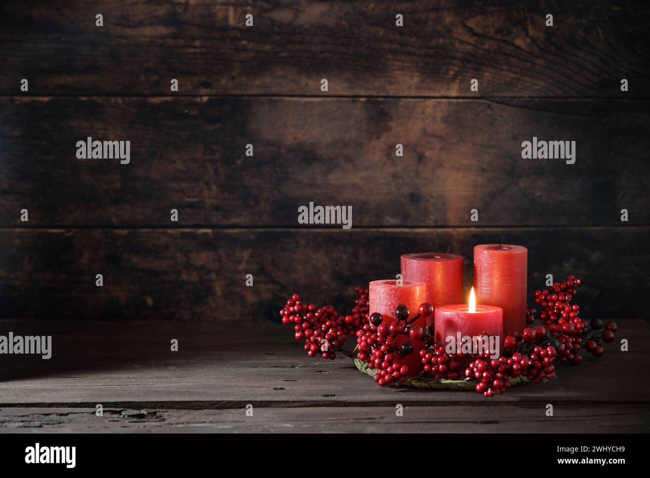 Frist Advent with red berry decoration and candles in a wreath, one is lighted, holiday home decor against a dark rustic wooden Stock Photo