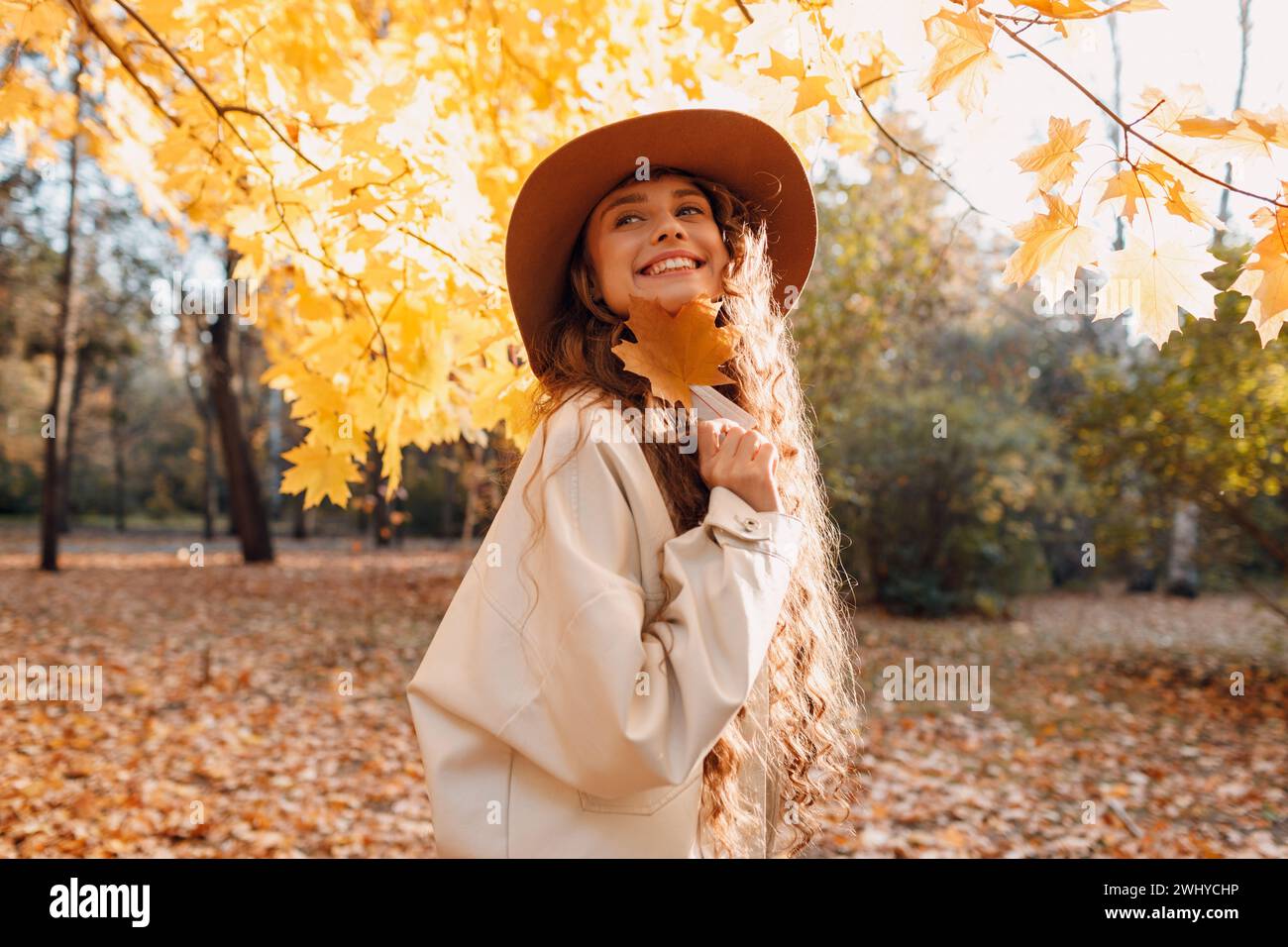 Smiling young woman portrait in the autumn forest with the yellow leaves at sunset. Stock Photo