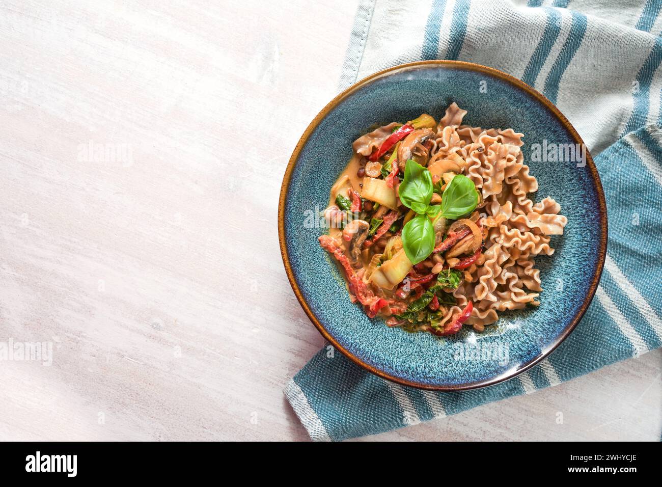 Healthy dish from wholemeal spelt pasta with vegetables in tomato sauce and basil garnish in a blue plate on a white wooden tabl Stock Photo