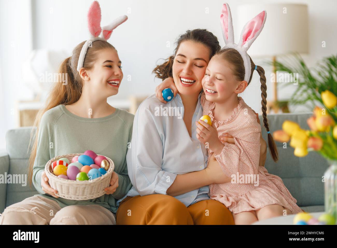 Happy holiday. Mother and her daughters with painting eggs. Family celebrating Easter. Cute little children girls are wearing bunny ears. Stock Photo