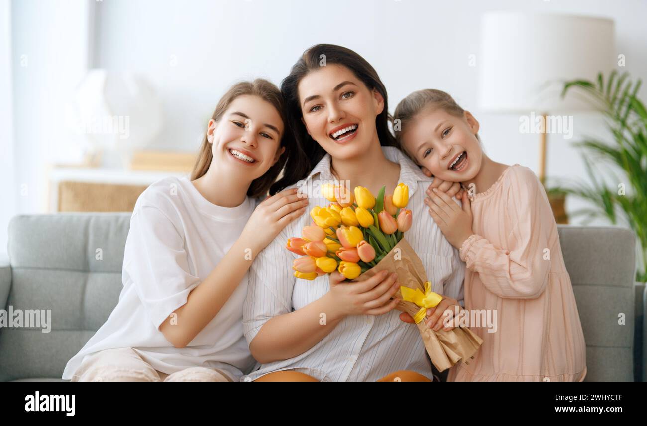 Happy mother's day. Children daughters are congratulating mom and giving her flowers. Mum and girls smiling and hugging. Family holiday and togetherne Stock Photo