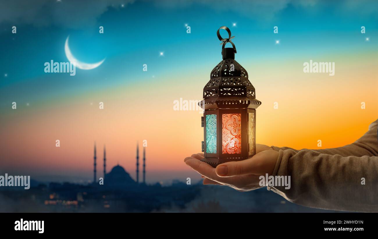 Ornamental Arabic lantern with burning candle glowing at night mosque background. Festive greeting card, invitation for Muslim holy month Ramadan Kare Stock Photo