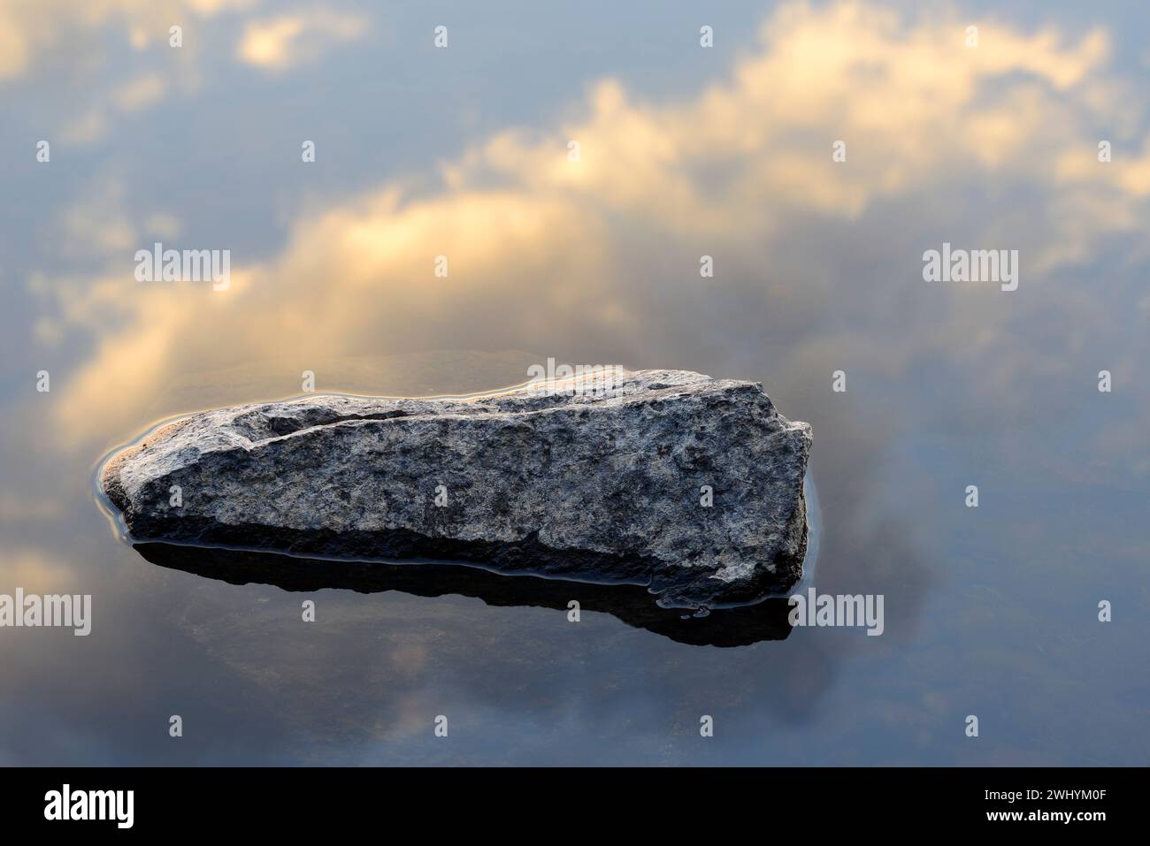 A stone in a lake and a reflection of clouds and sky in the water Stock Photo