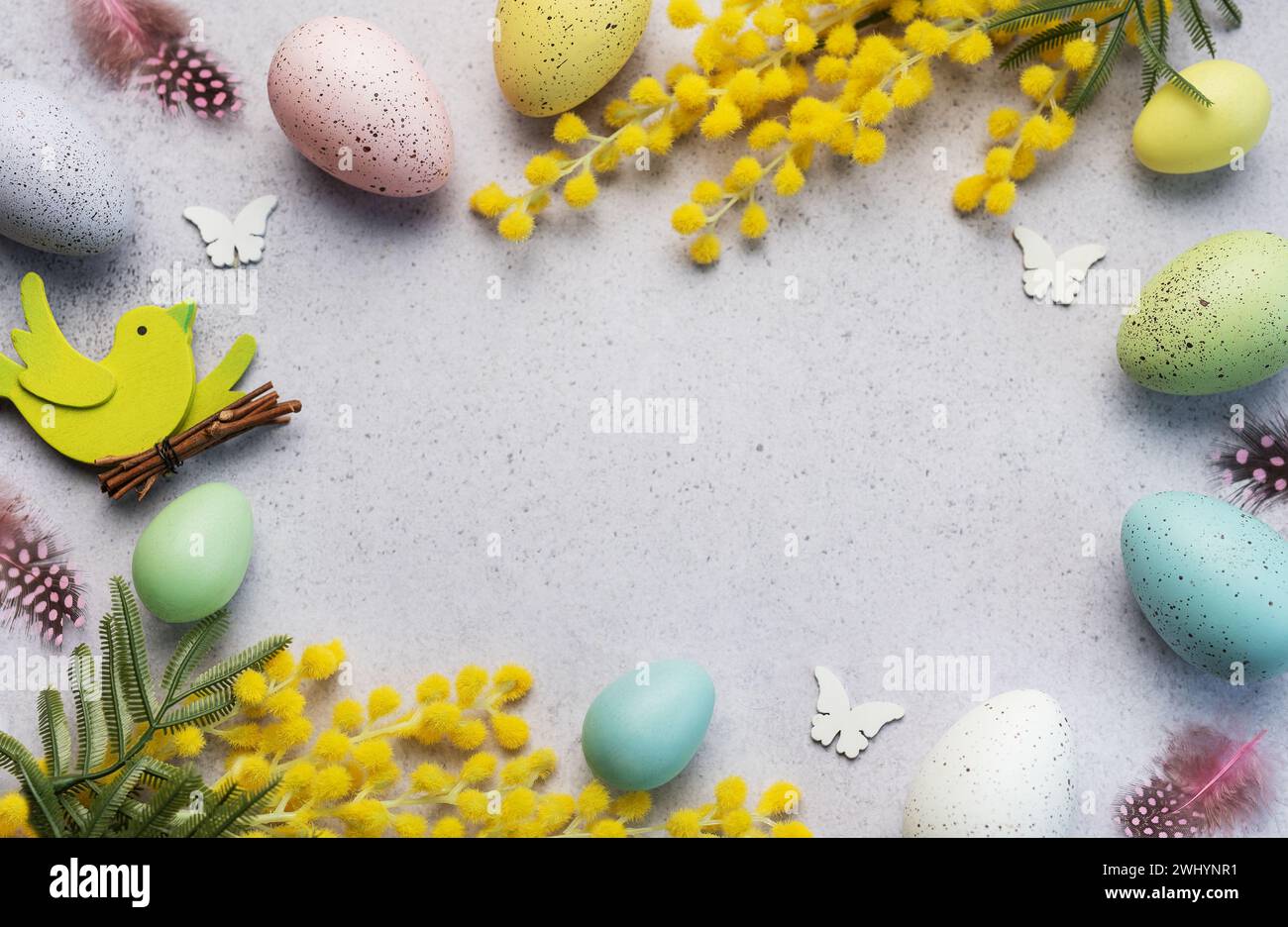 Decorative Easter composition featuring pastel-colored eggs, vibrant mimosa branches, and festive cutouts on a light, textured surface. Stock Photo