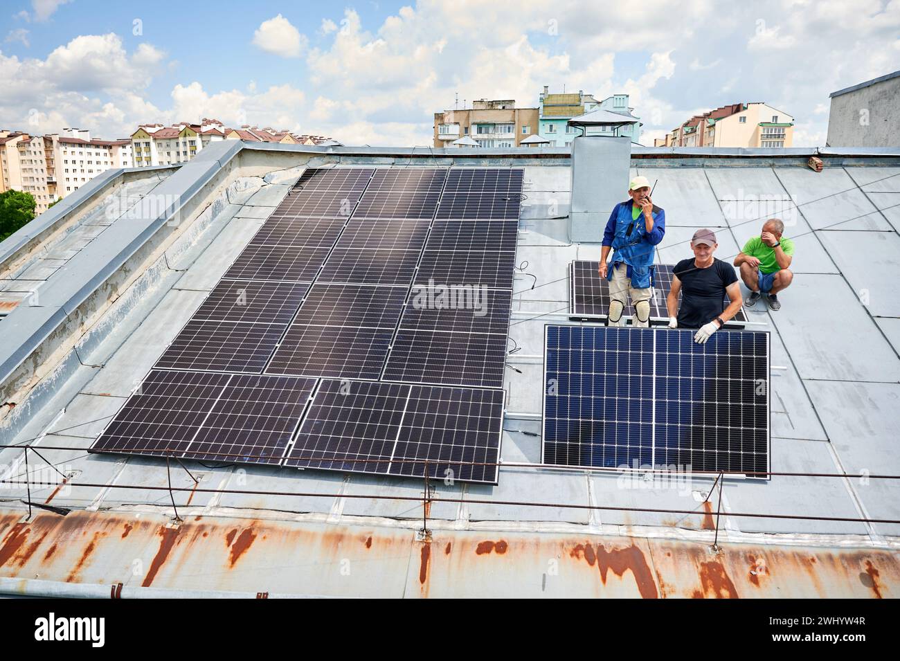 Workers building solar panel system on metal rooftop of house. Three men installers installing photovoltaic solar module outdoors. Alternative, green and renewable energy generation concept. Stock Photo