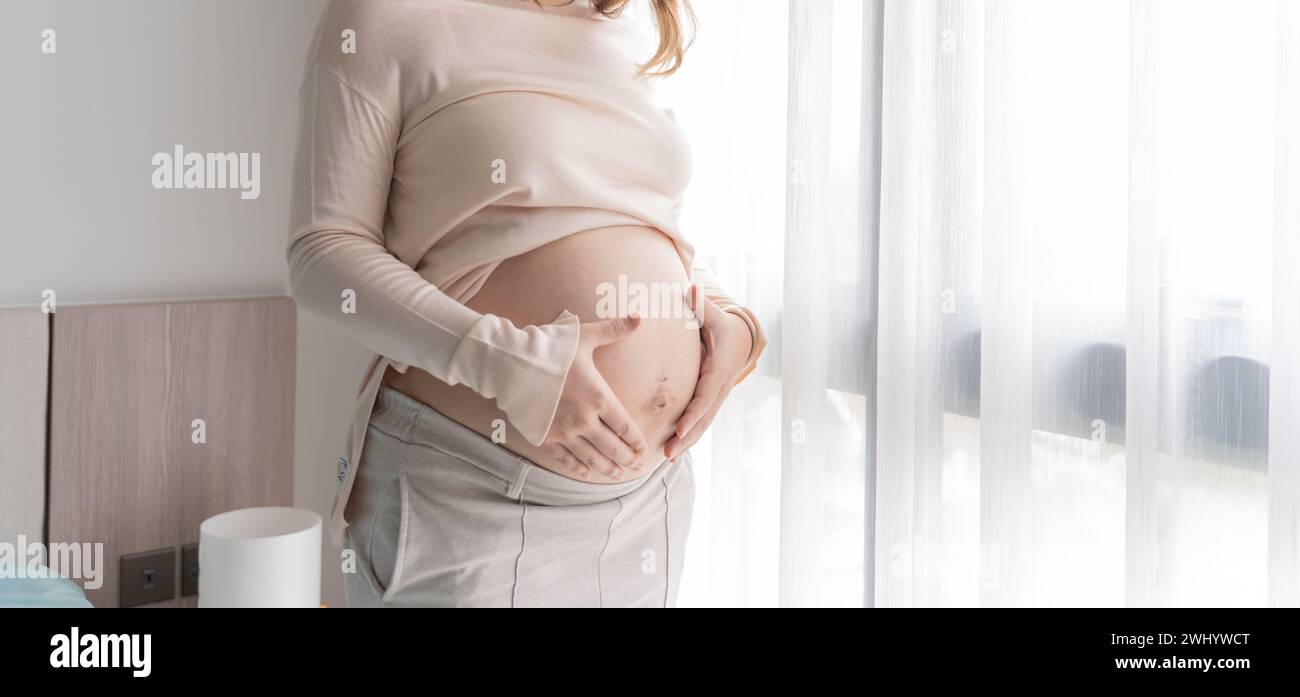 Pregnant woman holds hands on belly touching her baby caring about her health Beautiful happy pregnant womanÂ  tender mood photo Stock Photo
