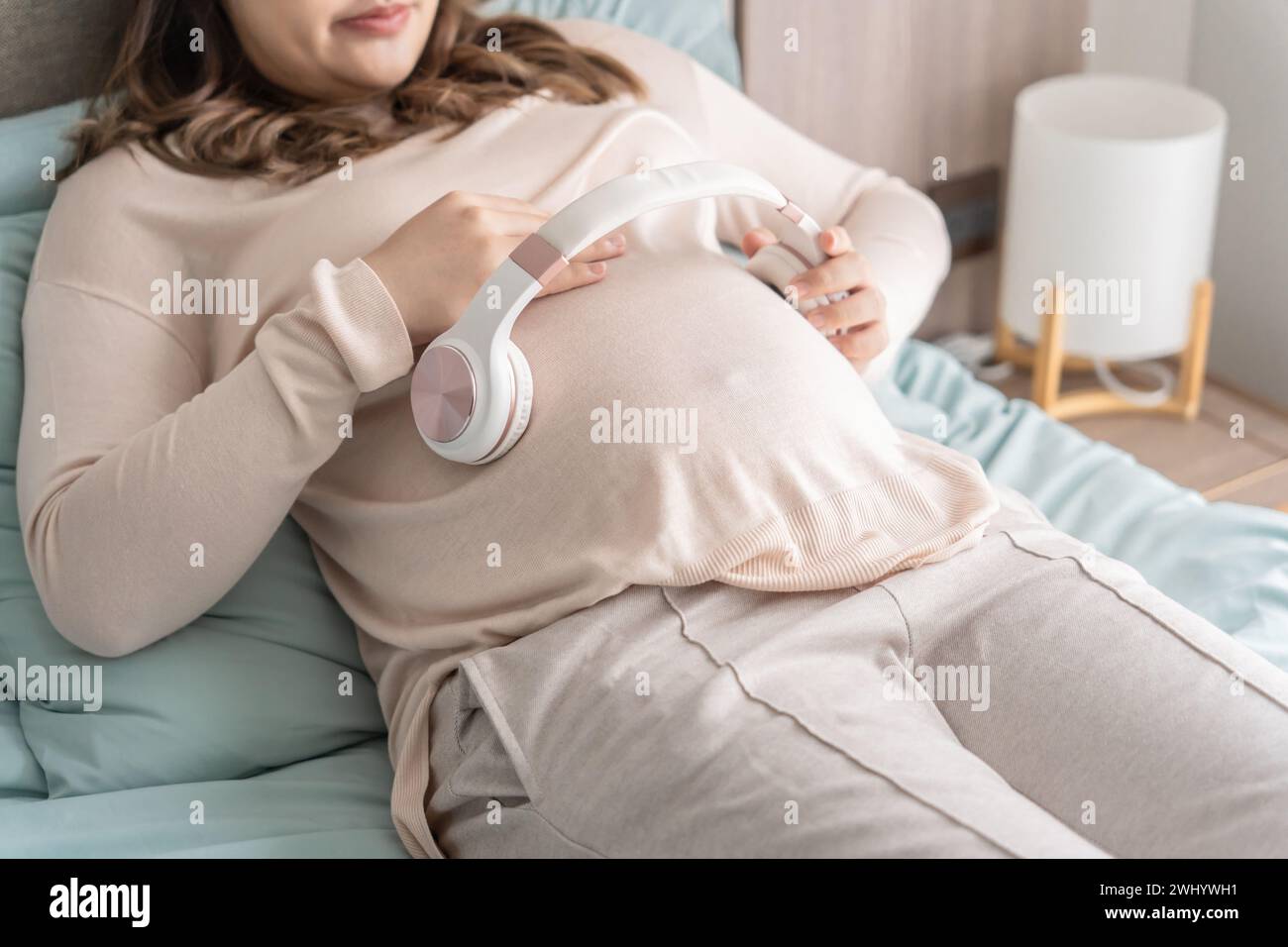 Pregnant asian woman holding headphone on belly playing music to her baby in stomach relaxing pregnancy  Mental health concept Stock Photo