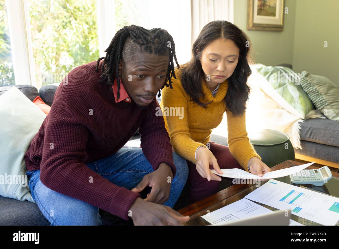 Serious diverse couple on couch using laptop discussing bills and domestic finances in living room Stock Photo