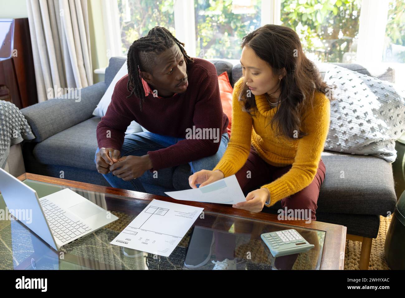 Serious diverse couple using laptop sitting on couch discussing bills and finances in living room Stock Photo