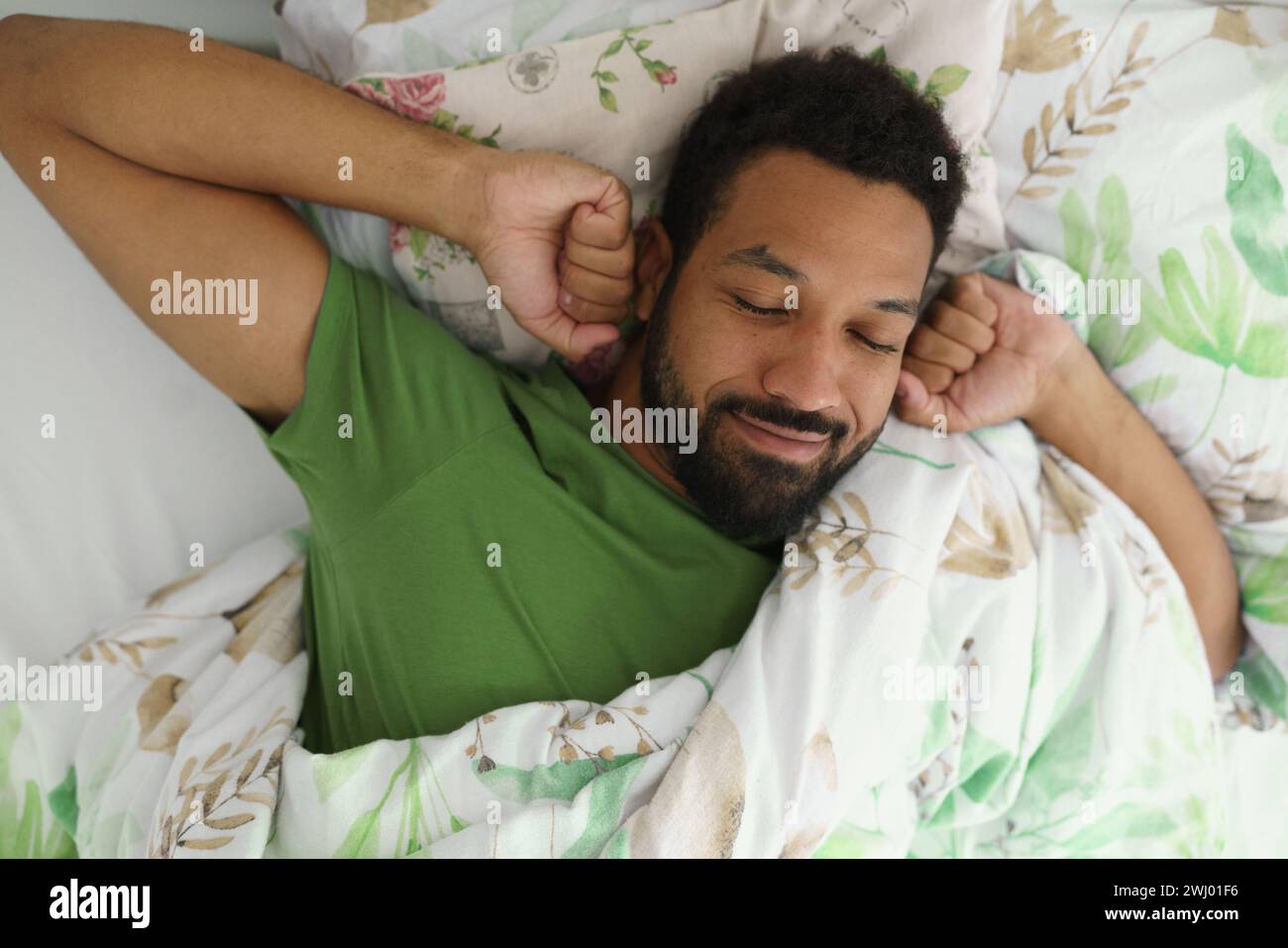 Top view of man waking up in bed, stretching arms, smiling in the morning. Stock Photo
