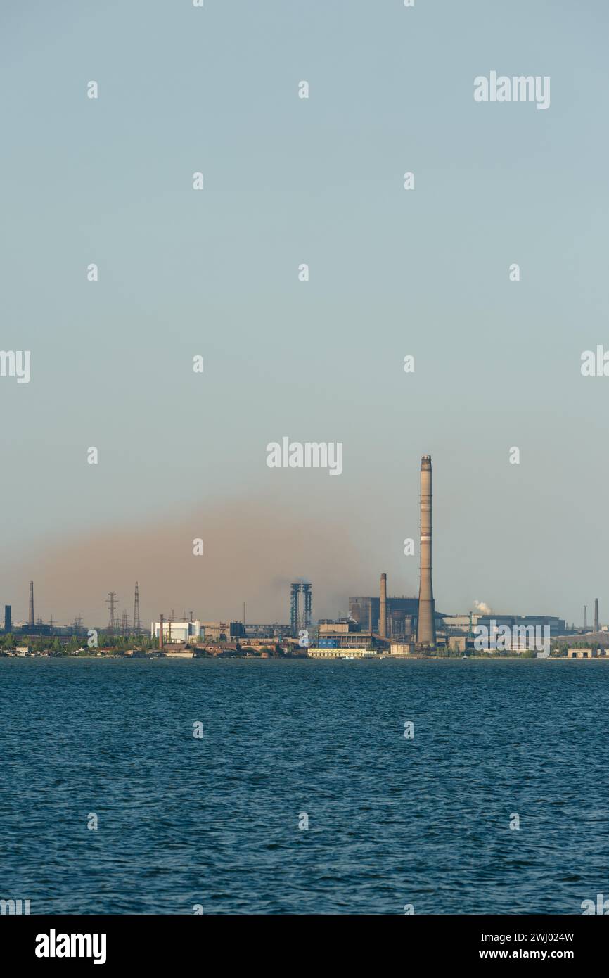 Industrial skyline dominated by a metallurgical plants tall chimneys emitting smoke over a body of water, symbolizing industrial pollution and eco Stock Photo