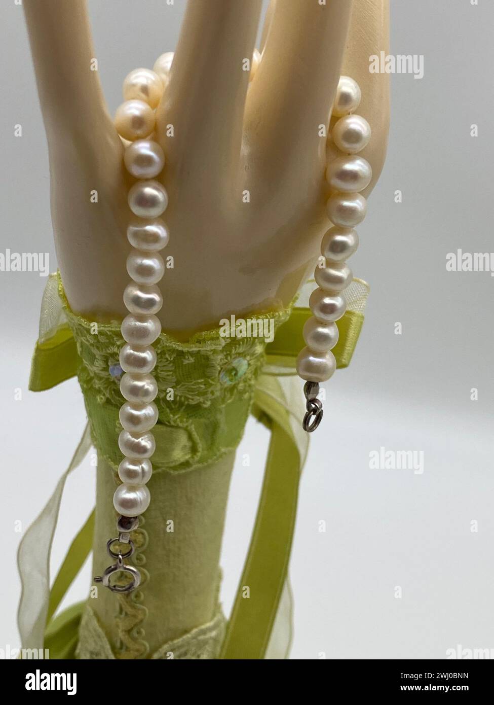 Close-up of a delicate doll's hand gently grasping a beautiful necklace Stock Photo
