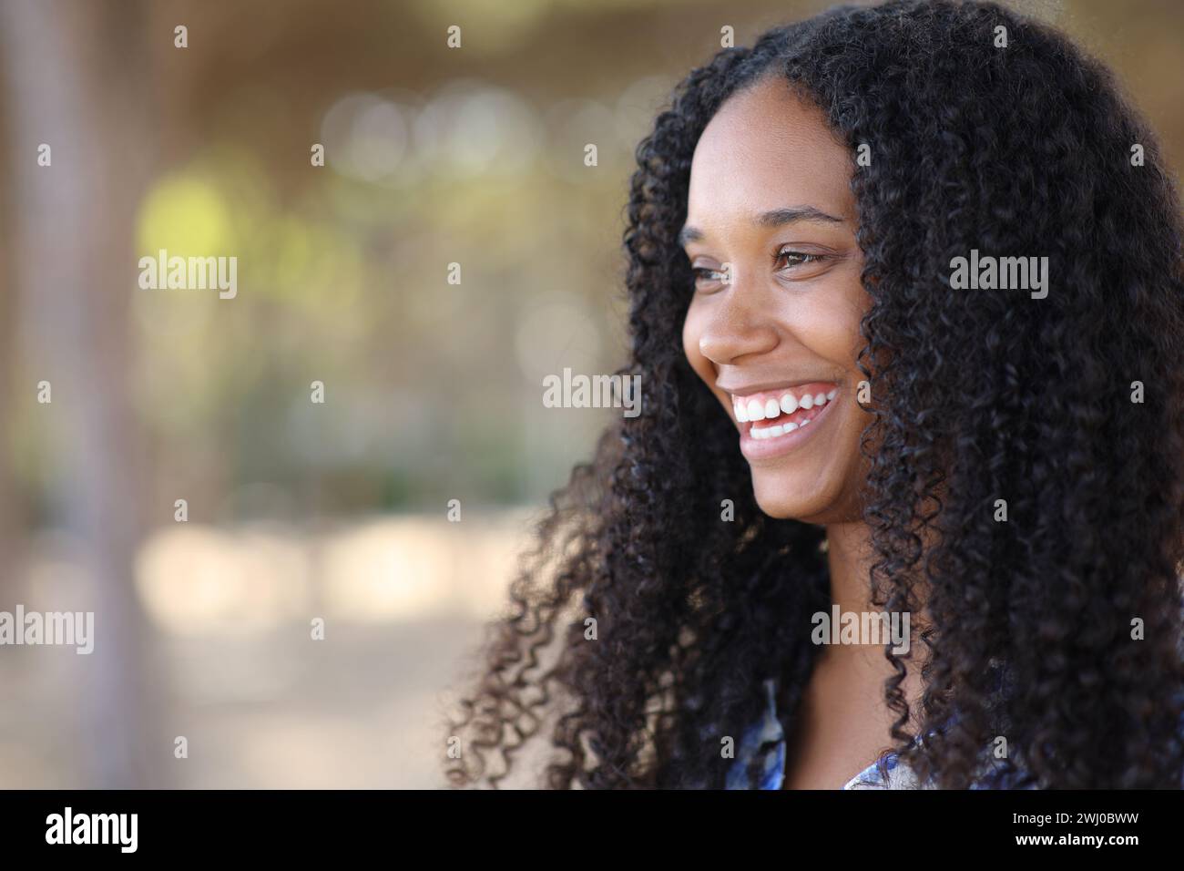 Happy black woman smiling with perfect teeth looking at side in a park Stock Photo