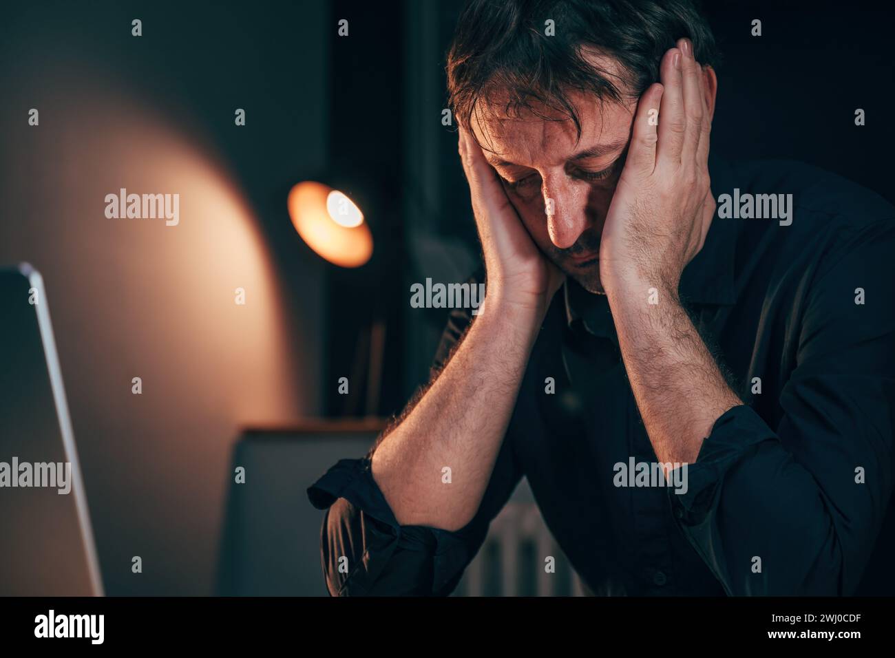 Headache at work, exhausted businessman sitting at office desk with severe head pain while working overtime, selective focus Stock Photo