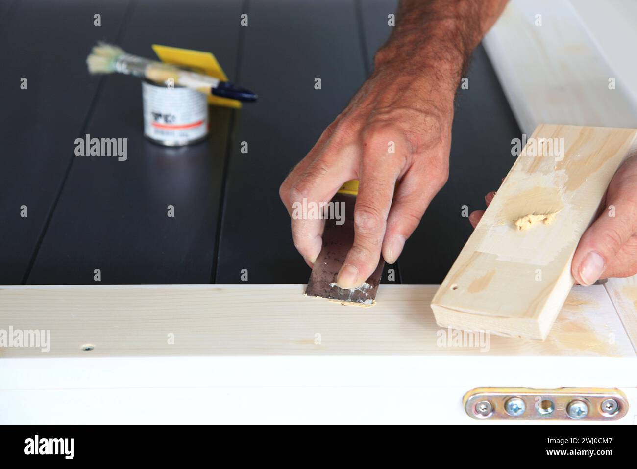 Putty knife in man's hand. DIY worker applying filler to the wood